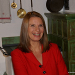 Zuhal Soyhan lächelt in rotem Outfit vor einer grünen Küchenzeile.