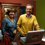 Zwei Personen an einem Empfangstresen mit Getränken und einem offenen Kassenbehälter.