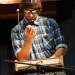 Mann mit Sonnenbrille und Mütze spielt auf einem ungewöhnlichen Instrument auf der Bühne.