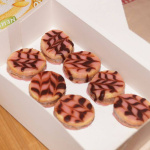 Bunte Kekse mit Zuckerglasur in einer weißen Schachtel auf Holzuntergrund.