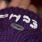 Lila Fingerhandschuh mit eingestickter Zahl und Markenschild, warme winterliche Stimmung.