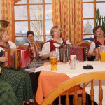 Bäuerinnen musizieren fröhlich mit Akkordeons in einem gemütlichen Gasthof.