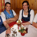 Vier Bäuerinnen in Tracht sitzen am Tisch und genießen die fröhliche Stimmung.