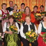 Bäuerinnen mit Blumenschmuck feiern gemeinsamen Humor beim Jahrtag in Saalfelden.