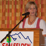 Bäuerin spricht am Mikrofon beim Event in Saalfelden, bunte Kulisse im Hintergrund.