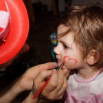 Ein Kind wird beim Kinderfasching mit einem roten Herz im Gesicht angemalt.