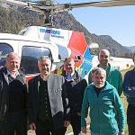 Gruppe von Männern vor einem Hubschrauber in einer bergigen Landschaft.