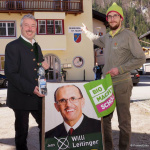 Zwei Männer stehen vor dem Gemeindehaus St. Martin mit Wahlplakat und Hinweis auf den Bürgermeister.