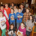Eine Gruppe von Kindern und Erwachsenen im Gemeindesaal, lächelnd mit Fastenspeisen.