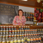 Marktfrau hinter einem Stand mit vielen Gläsern gefüllt mit eingelegtem Gemüse.