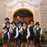 Junge Trachtenträger mit einem Erwachsenen vor dem Eingang des Gemeindeamts Lend.