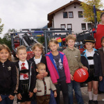 Kinder in traditionellen Trachten posieren fröhlich vor einer Veranstaltungsbühne.