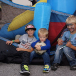 Drei Kinder posieren vor einem bunten Spielgerät, eines hält einen Fußball in den Armen.