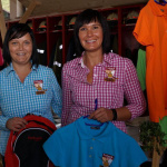 Zwei Frauen präsentieren bunte Polohemden, im Hintergrund Feuerwehrhelme und Rucksäcke.