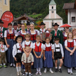 Traditionelle Trachtengruppe mit Akkordeon in Lend, umgeben von schöner Berglandschaft.