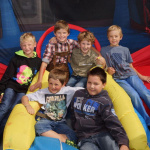 Sechs Kinder sitzen fröhlich in einer Hüpfburg und genießen einen sonnigen Tag.