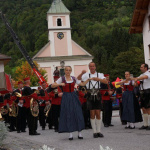 Traditionelles Fest mit Trachtenträgern und Blaskapelle in Lend, umgeben von malerischer Kulisse.