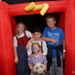 Kinder stehen fröhlich vor einem roten Hüpfburg-Eingang und halten einen Fußball.