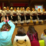 Tanzaufführung mit traditioneller Kleidung, begeisterte Kinder im Vordergrund.