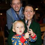 Familienmoment: Lächelnde Eltern mit ihrem freudigen Kind in festlicher Umgebung.